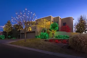 Beautiful Albuquerque home decorated with professional Christmas light installation, featuring colorful lights on trees, bushes, and the roofline.